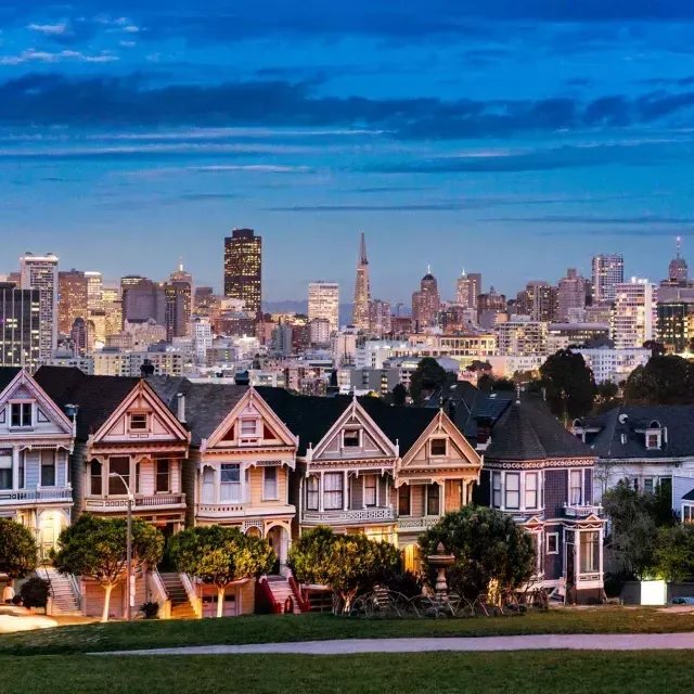 Die berühmten 画女士 vom Alamo Square sind in der Dämmerung vor der Skyline von San Francisco zu sehen.